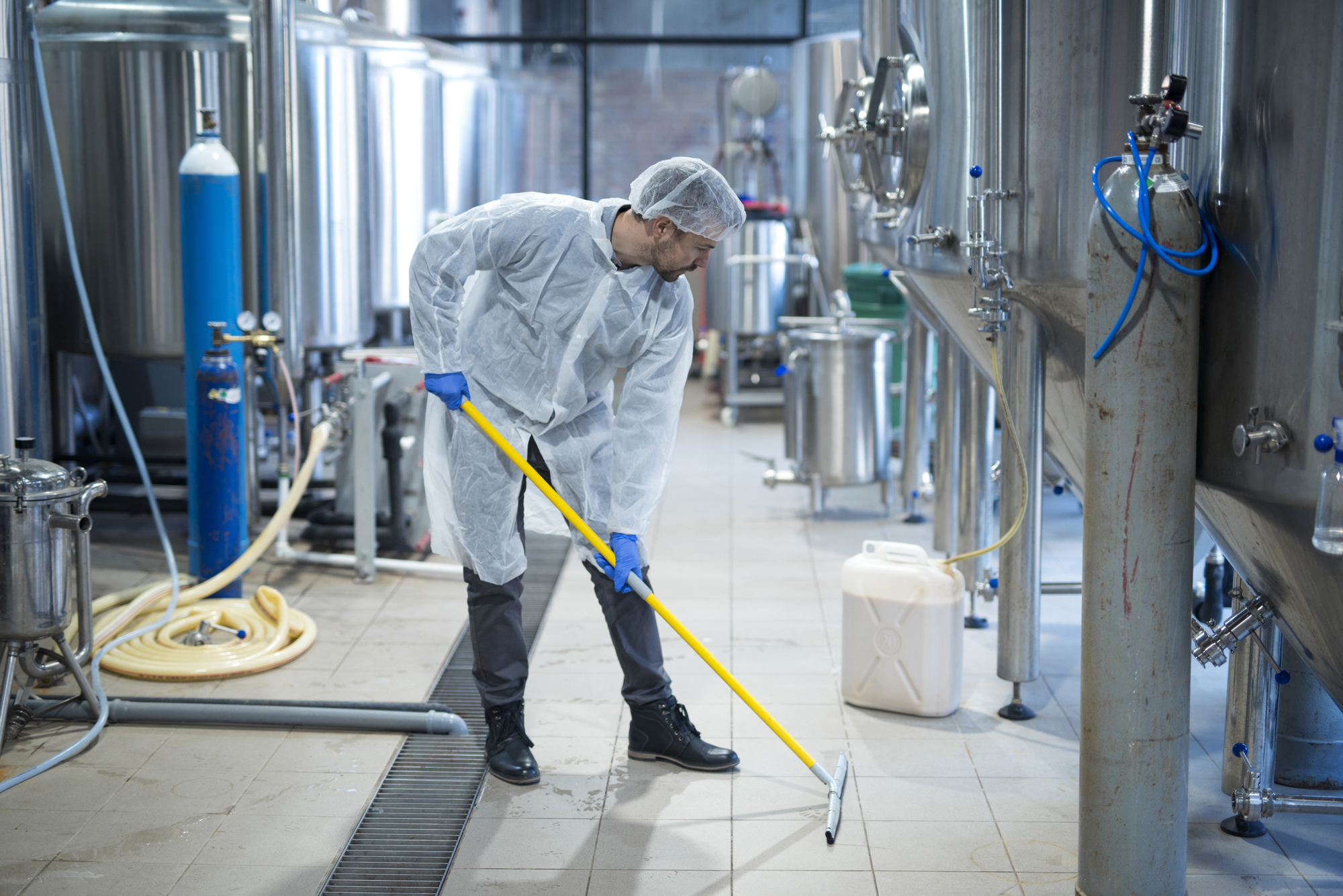 Food Sanitation Worker Surrounded by Metal Containers Mopping Floor